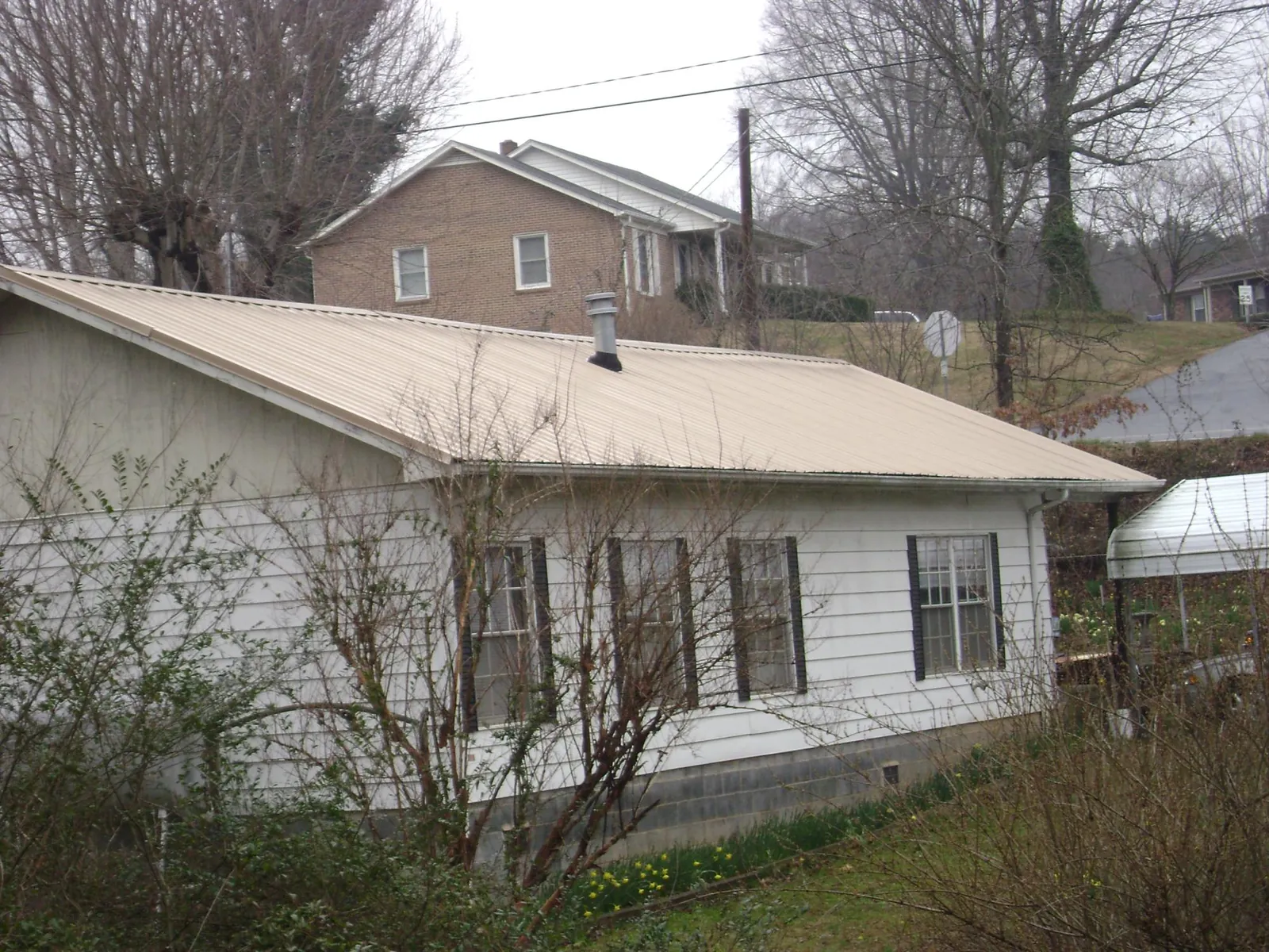 Tan metal roof on a white sided house set into a hillside — Commercial Roofing by Roofing Brothers in Cottonwood